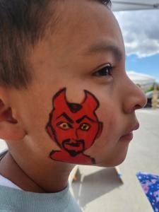 A young boy has a devil face painted on his face.