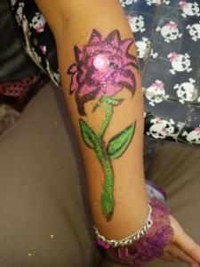 A girl has a tattoo of a pink flower on her arm.