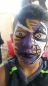 A young boy with his face painted in purple and yellow.