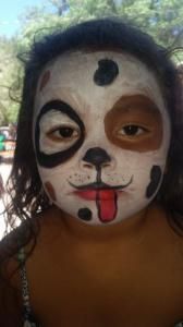 A little girl with her face painted like a dog with her tongue out.