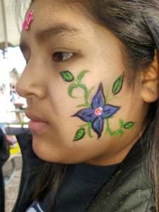 A young girl has a flower painted on her face.