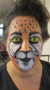 A woman with her face painted like a cheetah with green eyes.