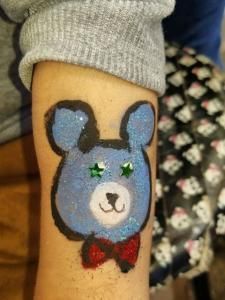 A person has a teddy bear face painted on their leg.