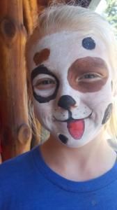 A young girl with her face painted like a dalmatian dog.