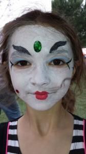 A woman with her face painted like a clown with a green emerald on her forehead.