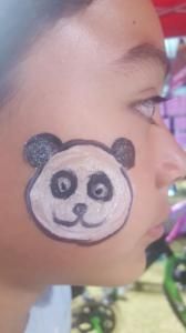 A child has a panda bear painted on their face.