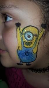 A little girl has a minion painted on her face.