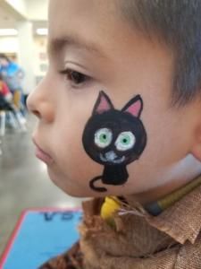 A young boy has a black cat painted on his face.