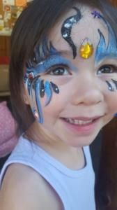 A little girl with face paint on her face is smiling.