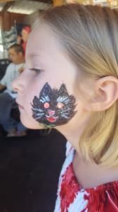 A little girl with a black cat painted on her face.