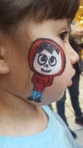 A little girl has a picture of coco painted on her face.