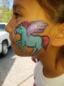A little girl has a unicorn painted on her face.