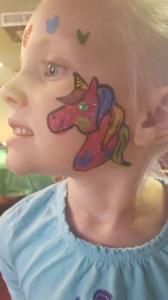 A little girl has a unicorn face painted on her face.