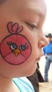 A little girl has an angry bird painted on her face.