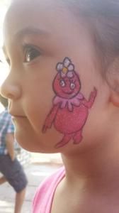 A little girl has a cartoon character painted on her face.