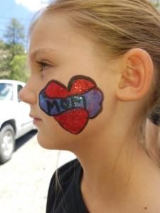 A young girl has a heart painted on her face that says mom