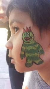 A young boy has a green monster painted on his face.