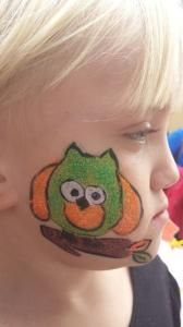 A little girl has an owl painted on her face.