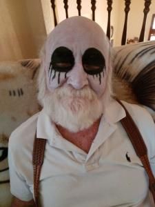 A man with a beard and makeup on his face is sitting on a couch.