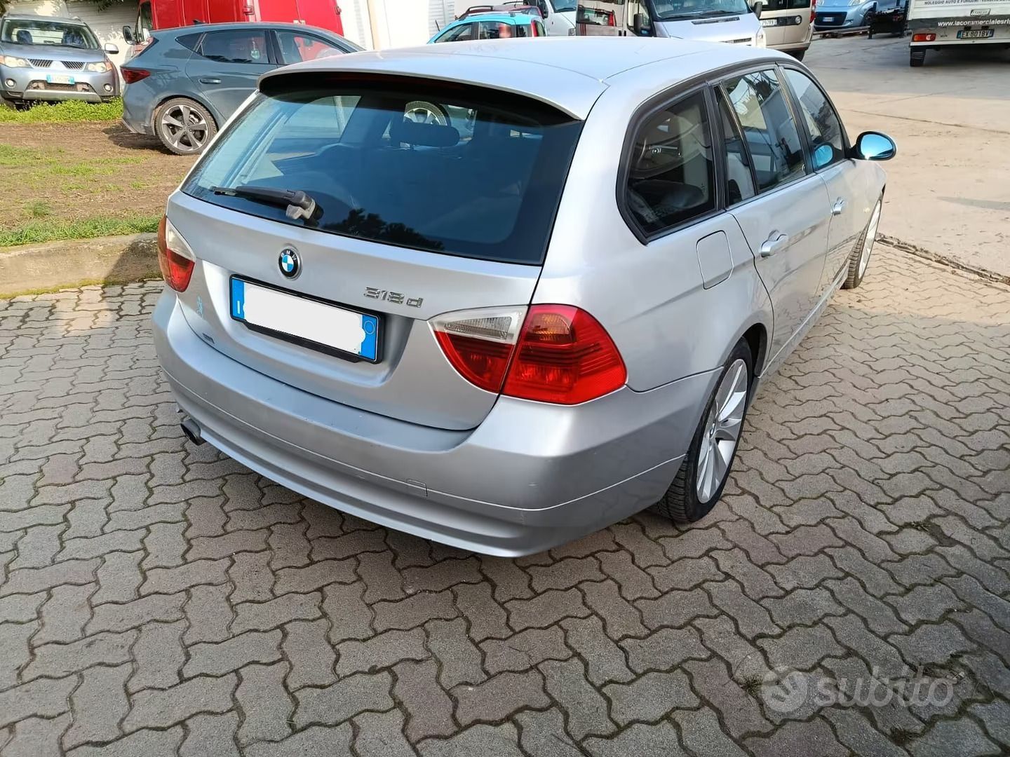 BMW hatchback argento parcheggiata su un piazzale pavimentato in mattoni, vista posteriore a tre quarti.
