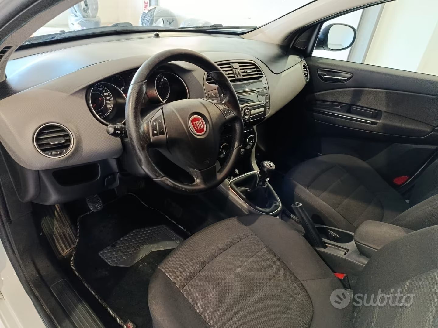 Interni dell'auto con sedili neri, volante Fiat e vista del cruscotto dal lato del guidatore.