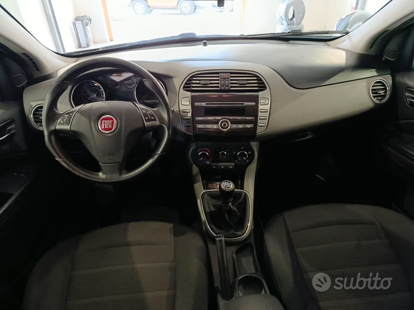 Vista interna del cruscotto di un'auto Fiat con volante, console centrale e sedili anteriori.