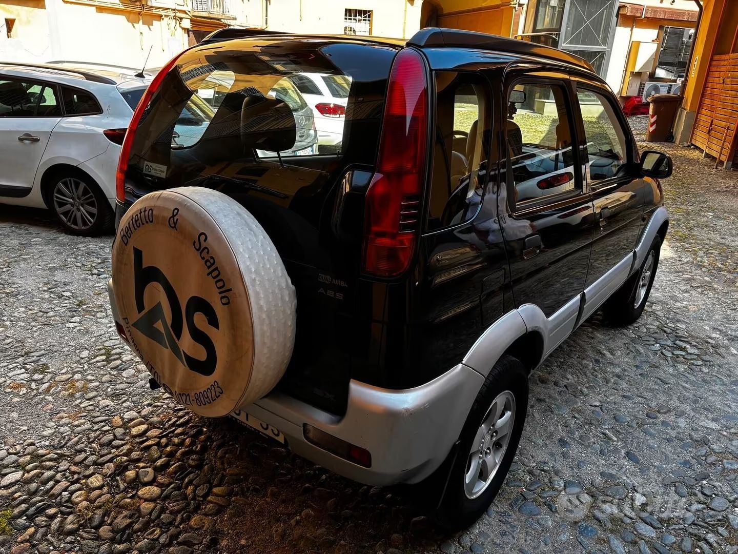 SUV compatto nero con ruota di scorta, parcheggiato in un garage soleggiato con un'altra auto nelle vicinanze.