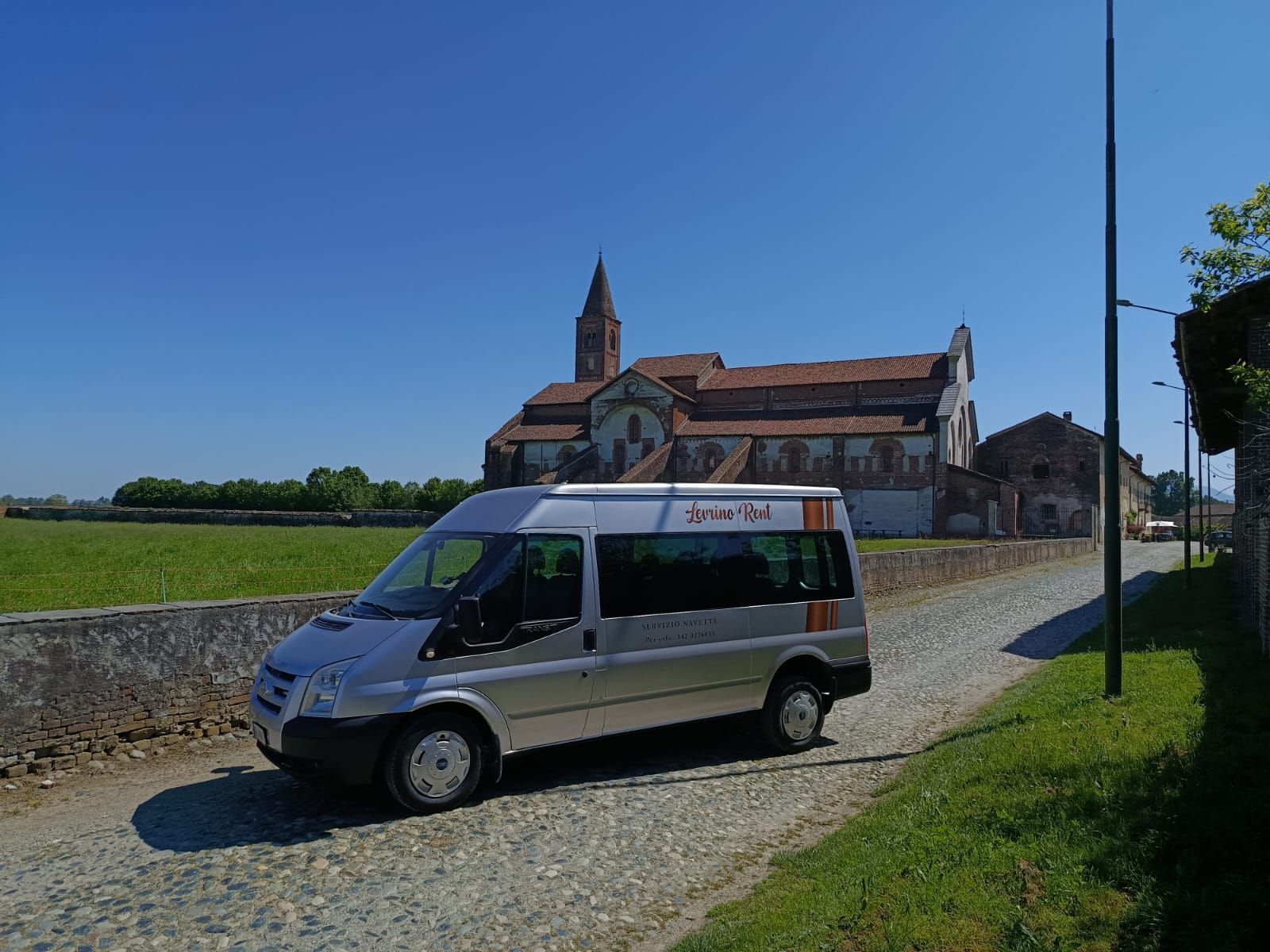 Furgone bianco parcheggiato in un soleggiato cortile storico circondato da edifici e archi in pietra.