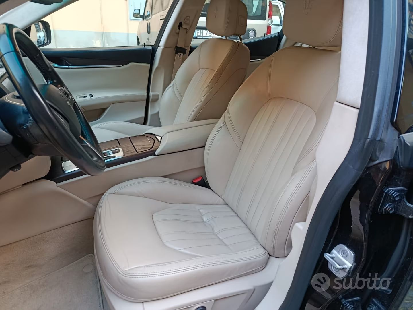 Interno dell'auto in pelle beige con sedili anteriori e console centrale, visto dal lato passeggero aperto