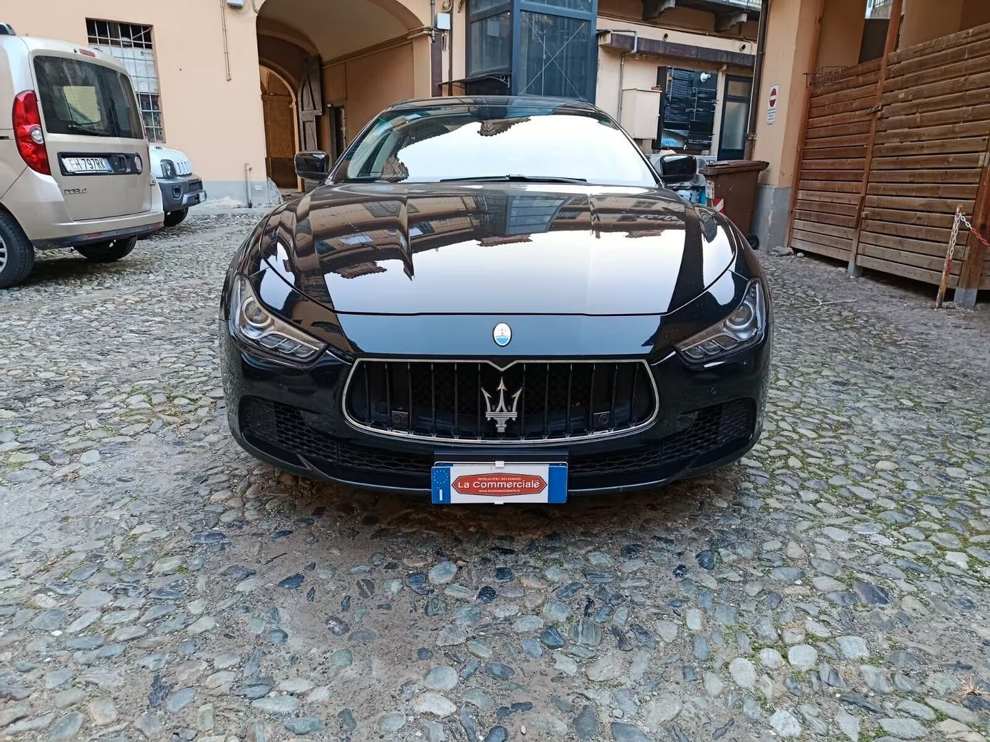 Maserati nera parcheggiata su una strada acciottolata tra gli edifici, vista frontale.