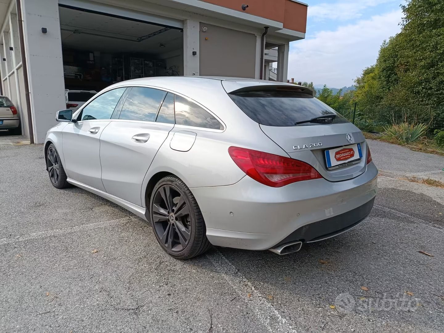 Una berlina Mercedes color argento è parcheggiata accanto a un edificio su un vialetto di ghiaia.