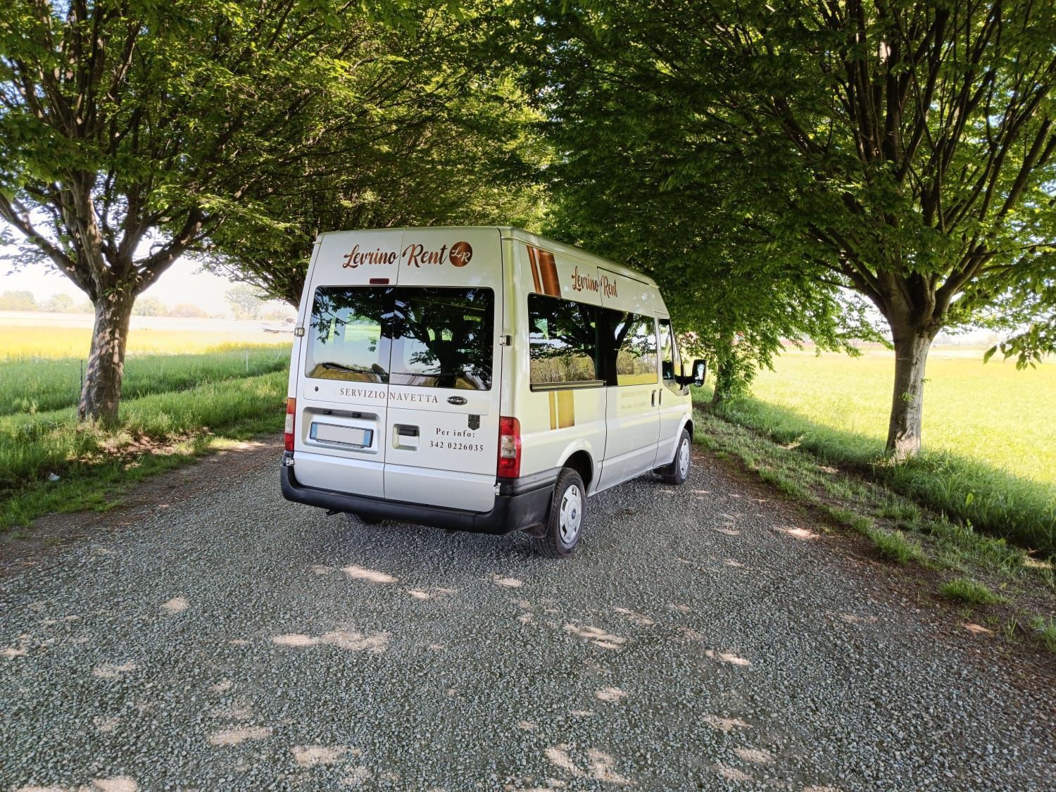 Furgone bianco parcheggiato su una strada sterrata alberata in un verde campo di campagna.
