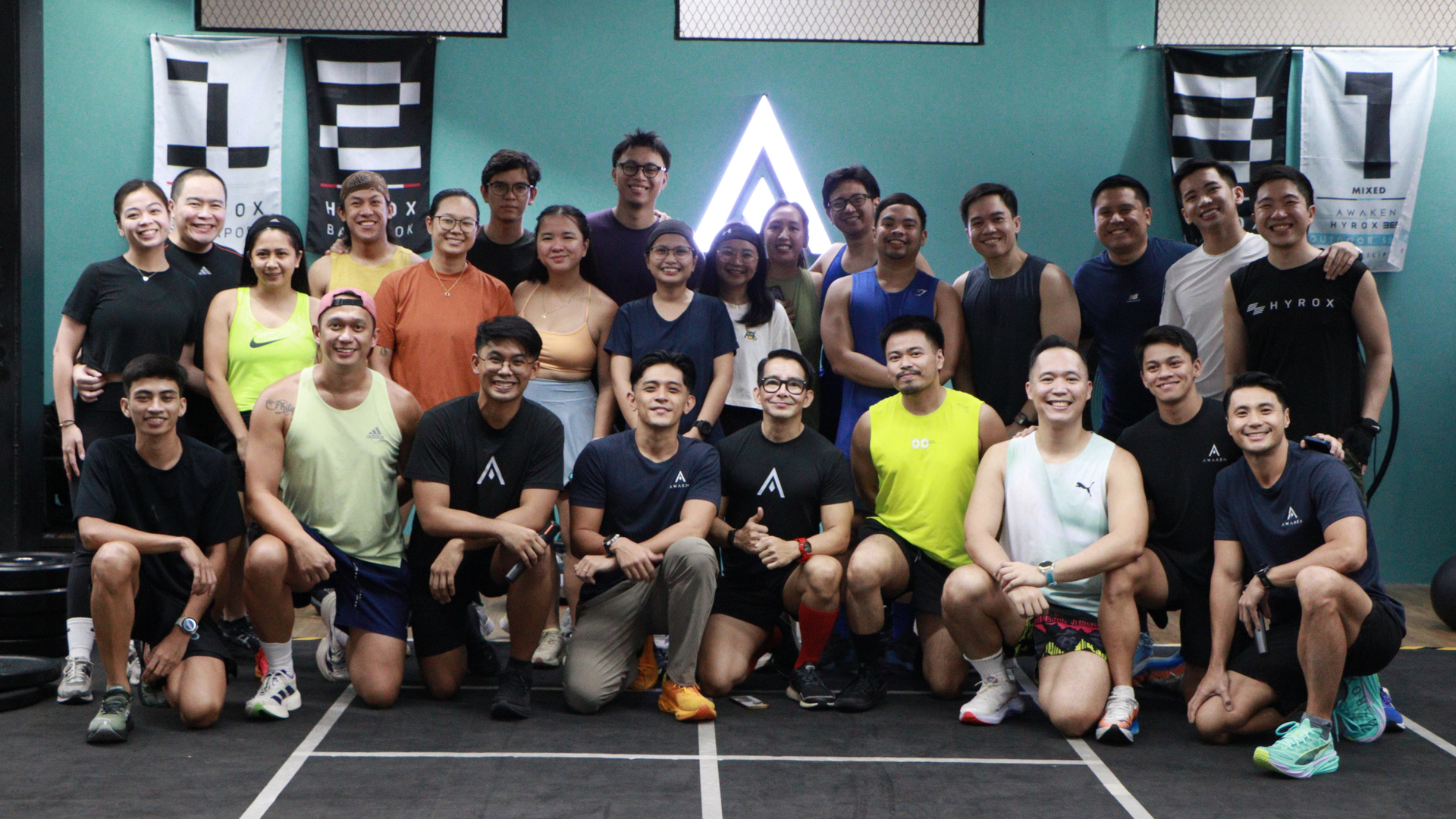 Group fitness class posing together in a gym, smiling in front of a large illuminated star logo.