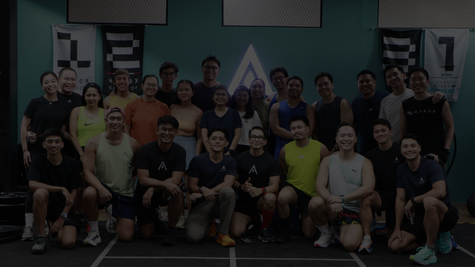 Group of people posing in a gym, some standing and some kneeling, in front of exercise equipment.