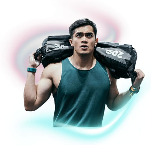 A person in a dark green tank top carrying a black sandbag on their shoulders against a soft, colorful light background.