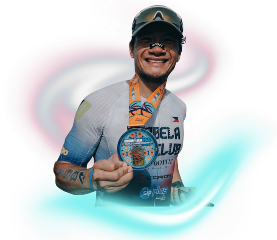 A person wearing a sports jersey and cap smiles while holding up a colorful circular medal against a blurry background.
