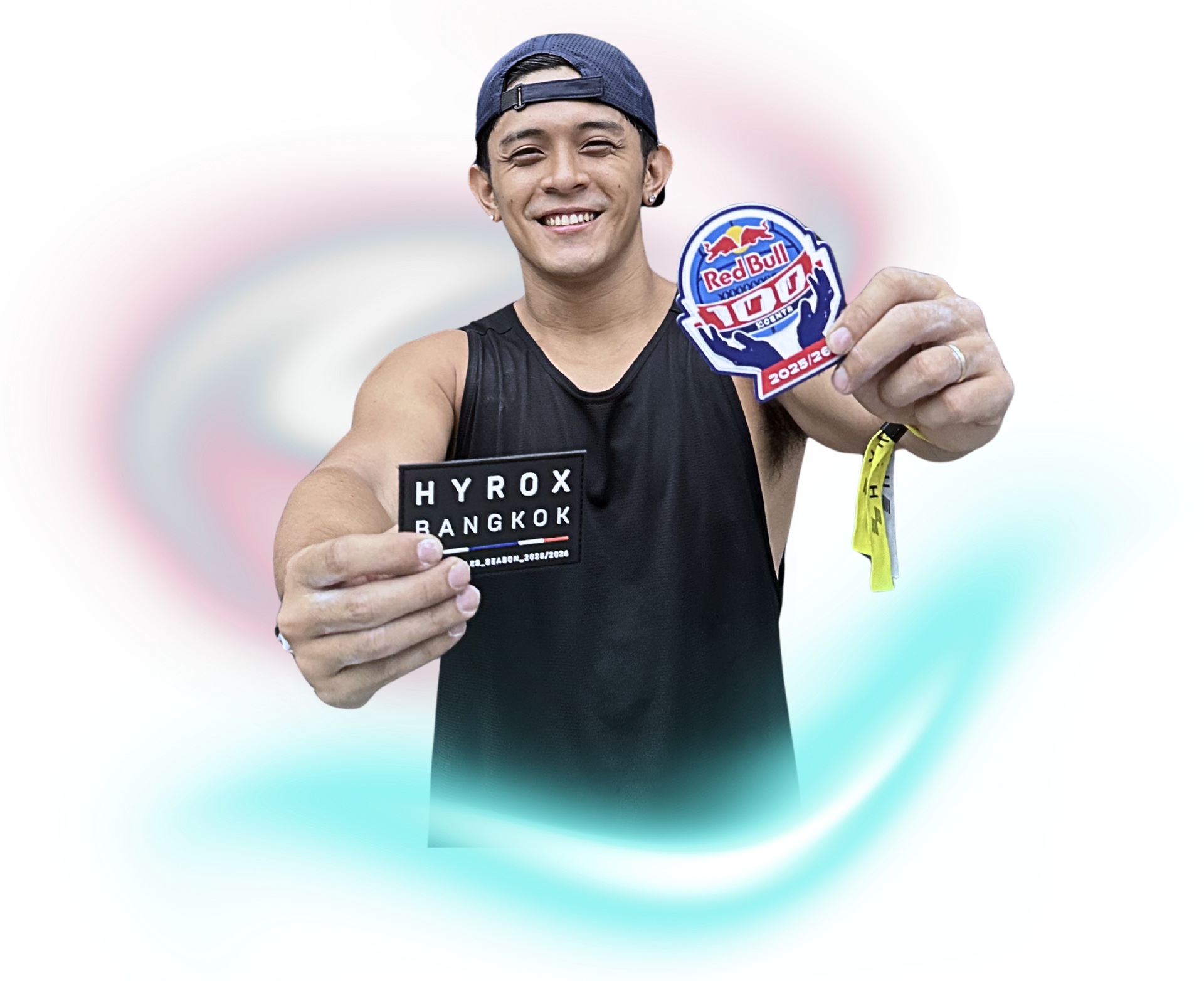 A smiling person holds a Hyrox Bangkok card in one hand and a Red Bull patch with a yellow wristband in the other.