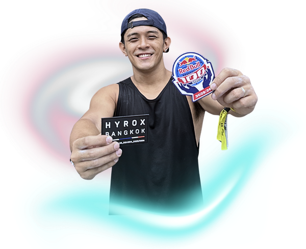 A smiling person holds a Hyrox Bangkok card in one hand and a Red Bull patch with a yellow wristband in the other.