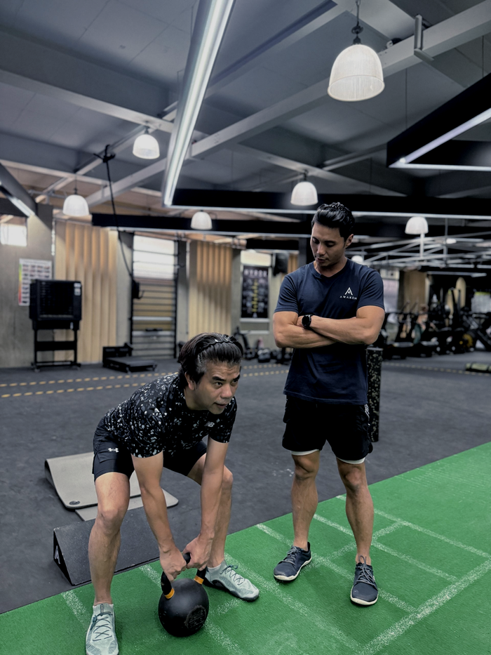 A fitness trainer observes a trainee performing a kettlebell exercise in a gym.