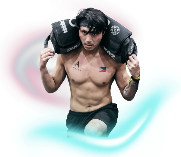 A shirtless athlete with a determined expression lifting a heavy sandbag across his shoulders against a white background.
