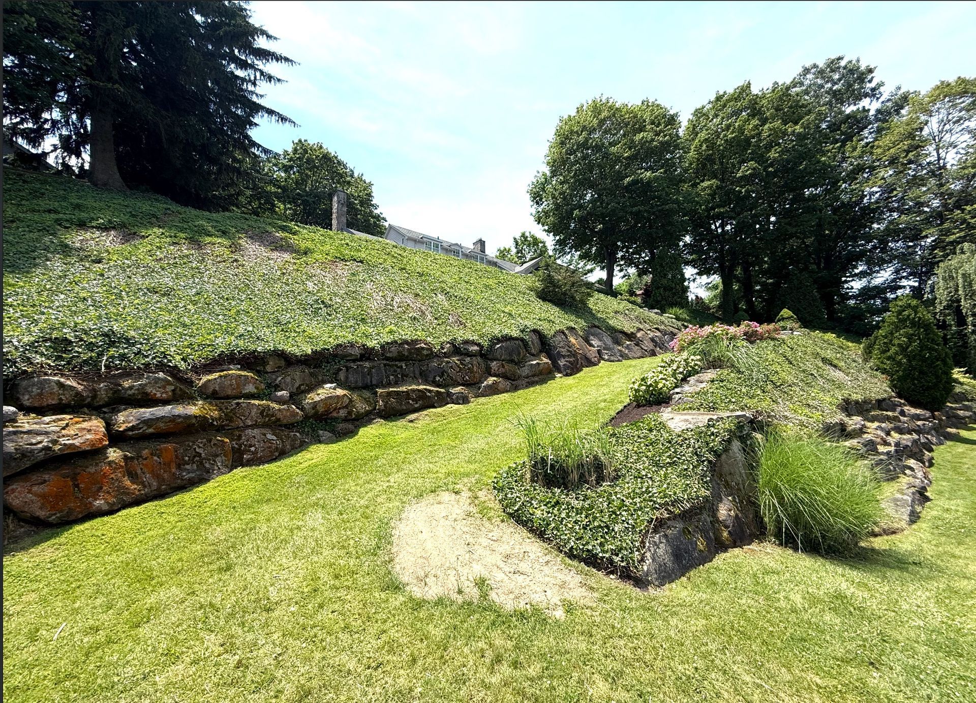 Stone retaining walls support a grassy hillside in a sunny park setting.