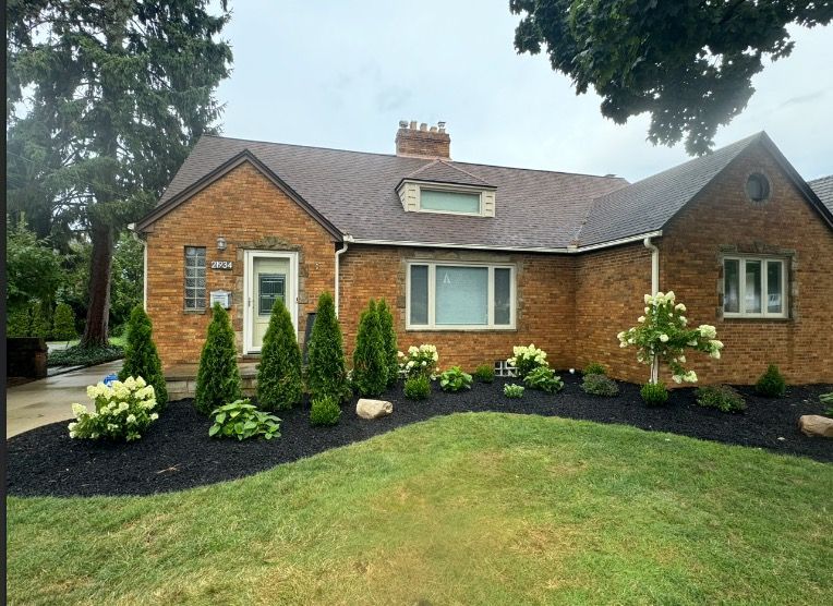 Brick house with manicured landscaping, including green lawn and black mulch flower bed with shrubs.