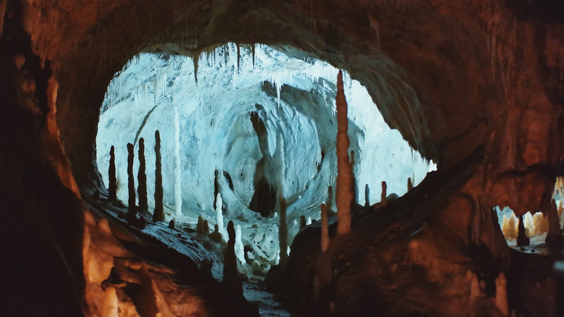 Cave interior with stalactites and stalagmites, lit with blue light, creating a glowing effect.
