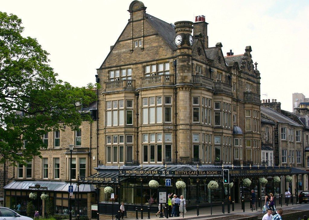 Stone building, hotel with ornate details, clock tower, and glass-covered entrance. People on sidewalk.