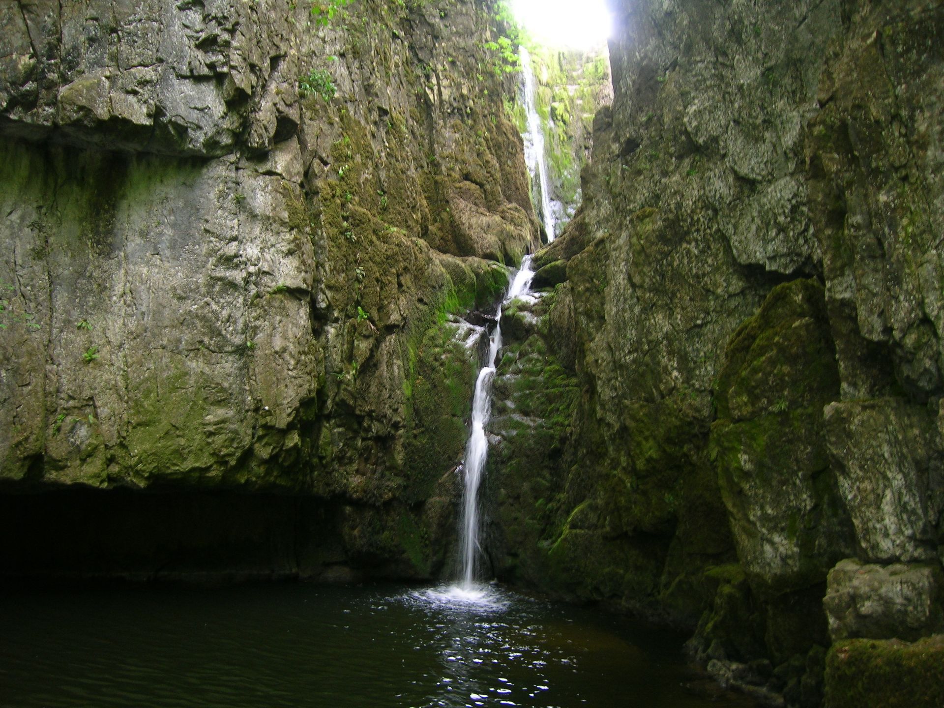 Waterfall cascading into a dark pool, flanked by moss-covered rock walls.