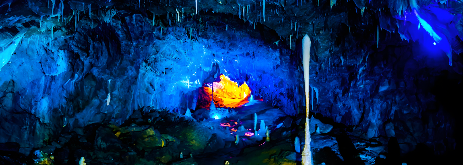 Cave interior lit with blue and orange lights, highlighting rock formations and a central glowing object.