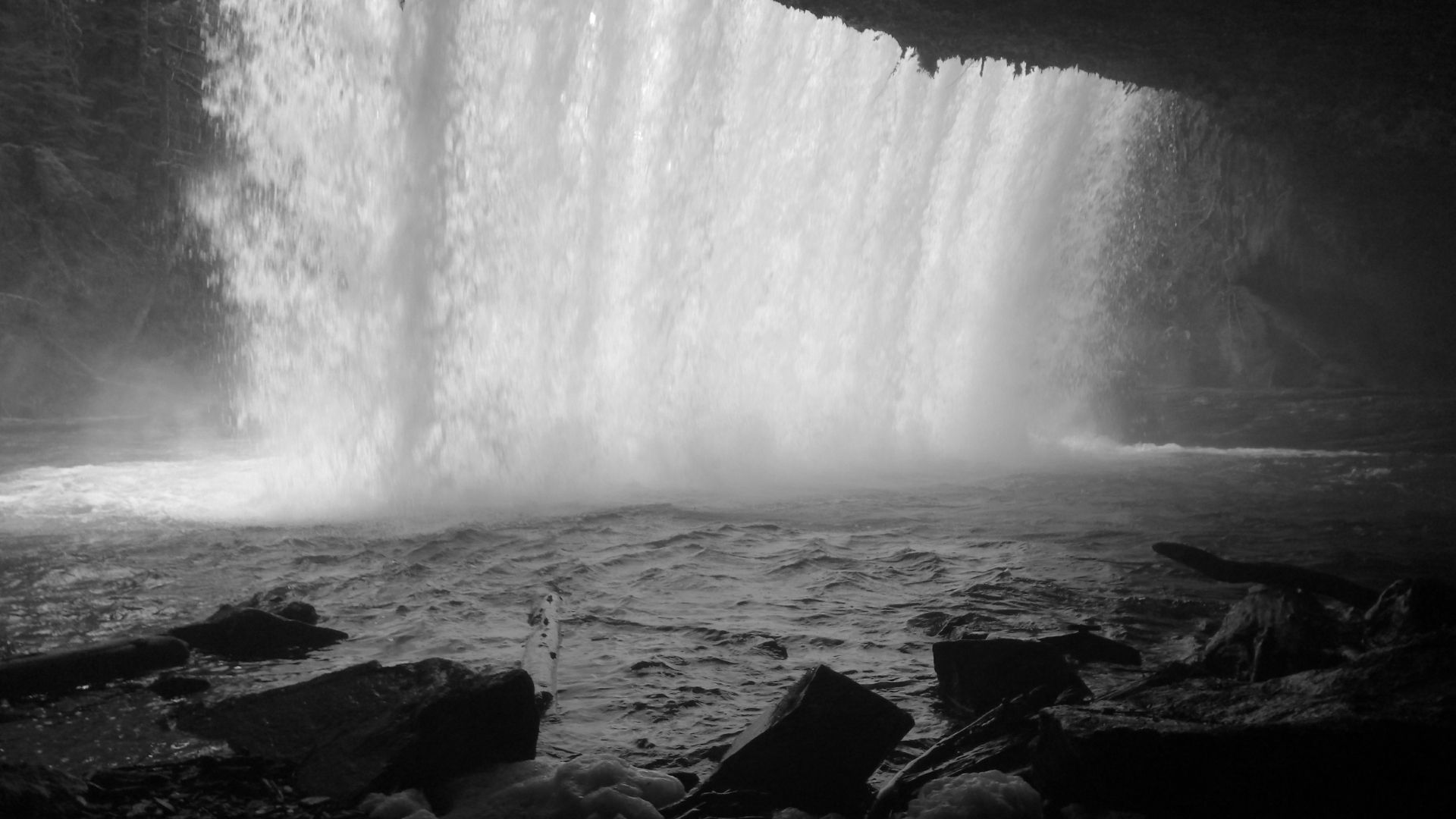 Waterfall cascading into a pool of water, rocks in foreground, dark cave setting.