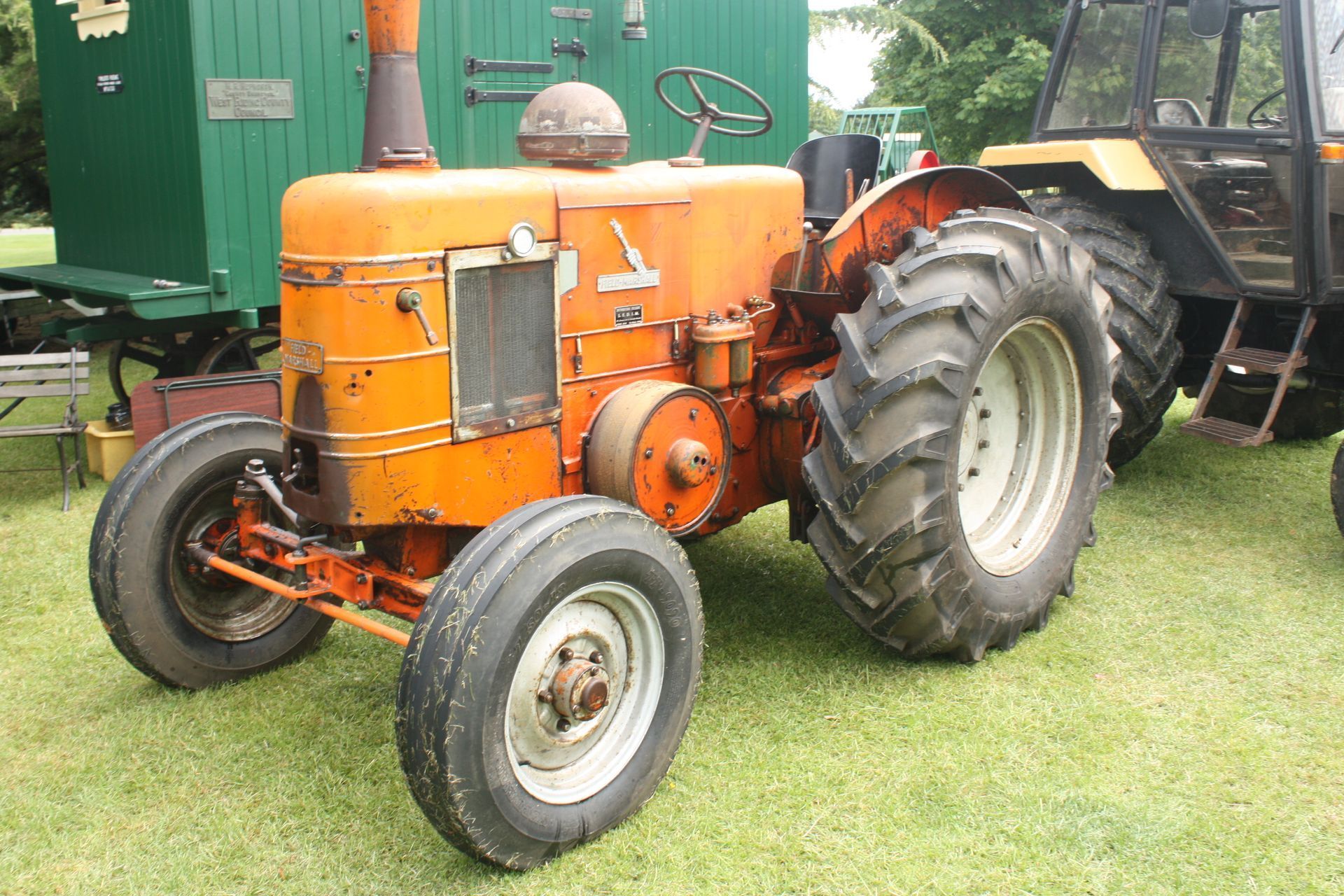 Orange vintage tractor on grass with a green structure in the background.
