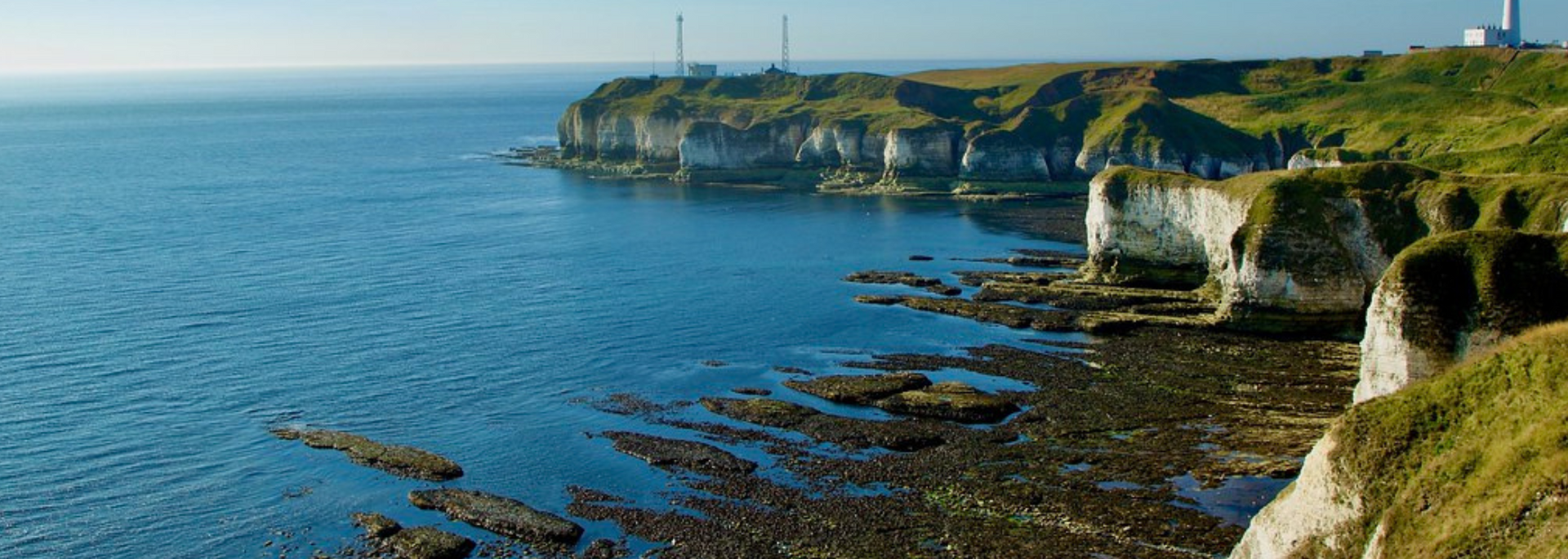 Coastal view with cliffs, ocean, and a lighthouse in the distance.