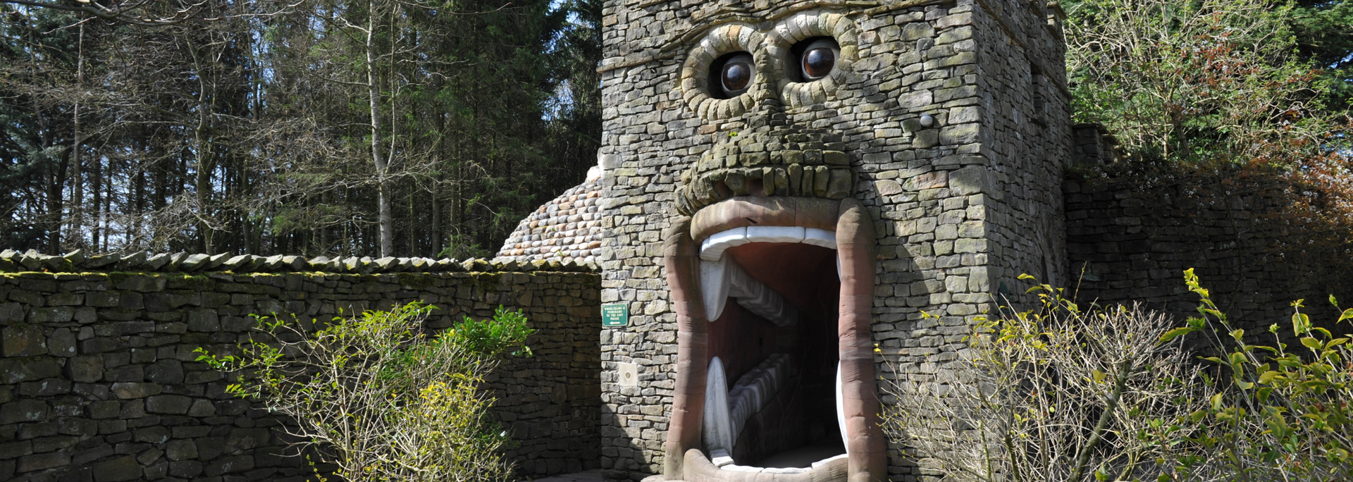 Stone structure with a large open mouth and eyes, resembling a monster's face. Surrounded by greenery.